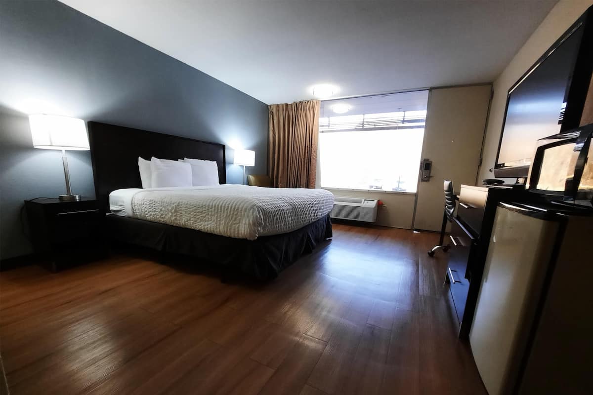 A hotel room with a bed, a desk, a chair, a refrigerator, and a window with curtains.