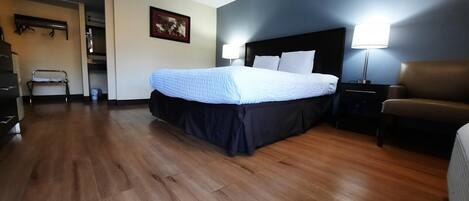 A hotel room with a bed, bedside lamps, a chair, and a wooden floor.