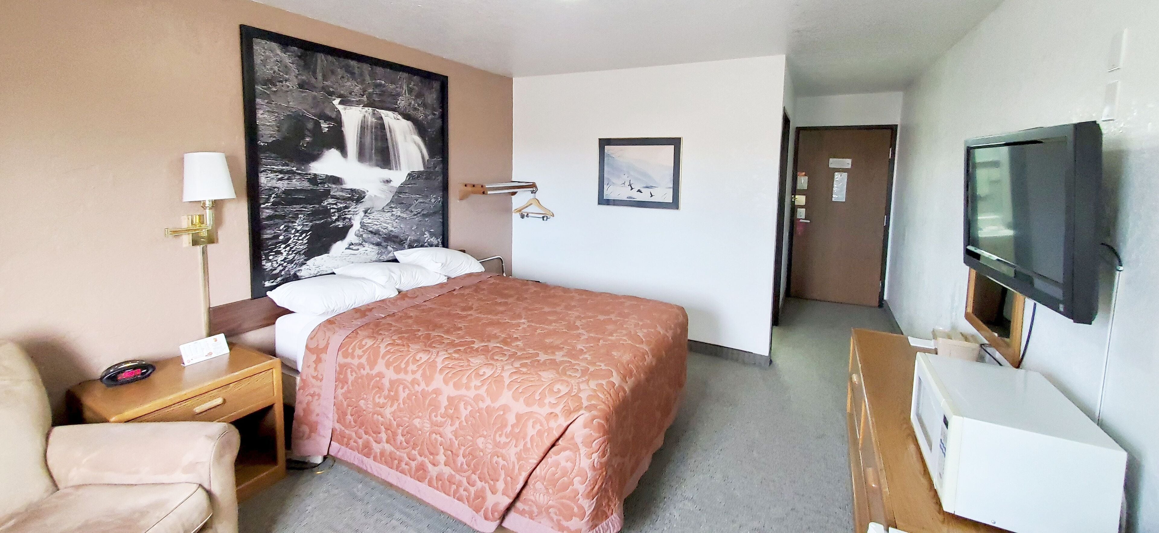 Habitación de hotel con cama, escritorio, silla, televisor y un cuadro grande en la pared.