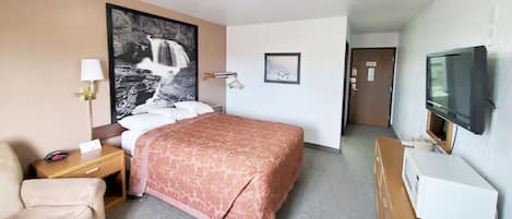 Habitación de hotel con cama, escritorio, silla, televisor y un cuadro grande en la pared.