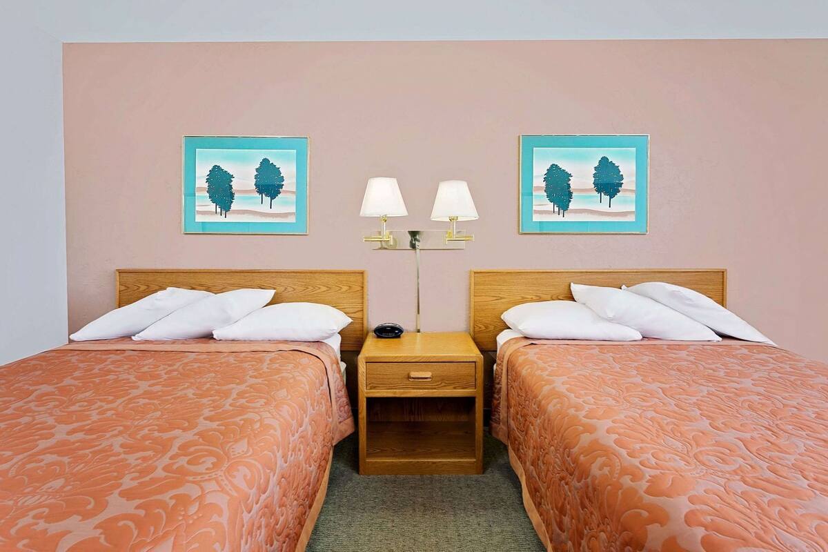 A hotel room with two beds, a nightstand, two wall-mounted lamps, and two framed pictures.