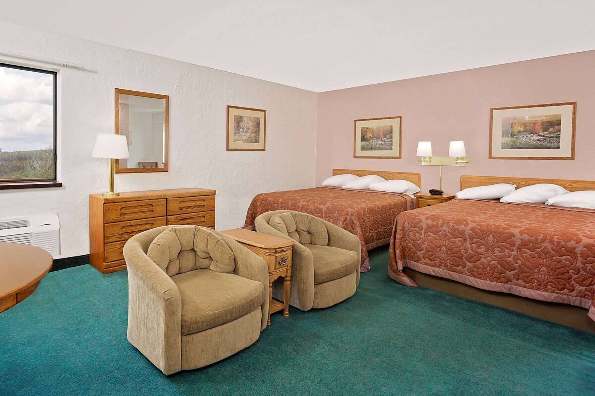 A hotel room with two beds, a wooden dresser, a chair, and a small table.