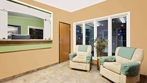 A room with two beige armchairs, a large mirror, a wooden door, and a window with frosted glass. - Super 8 by Wyndham Cut Bank (Cut Bank)