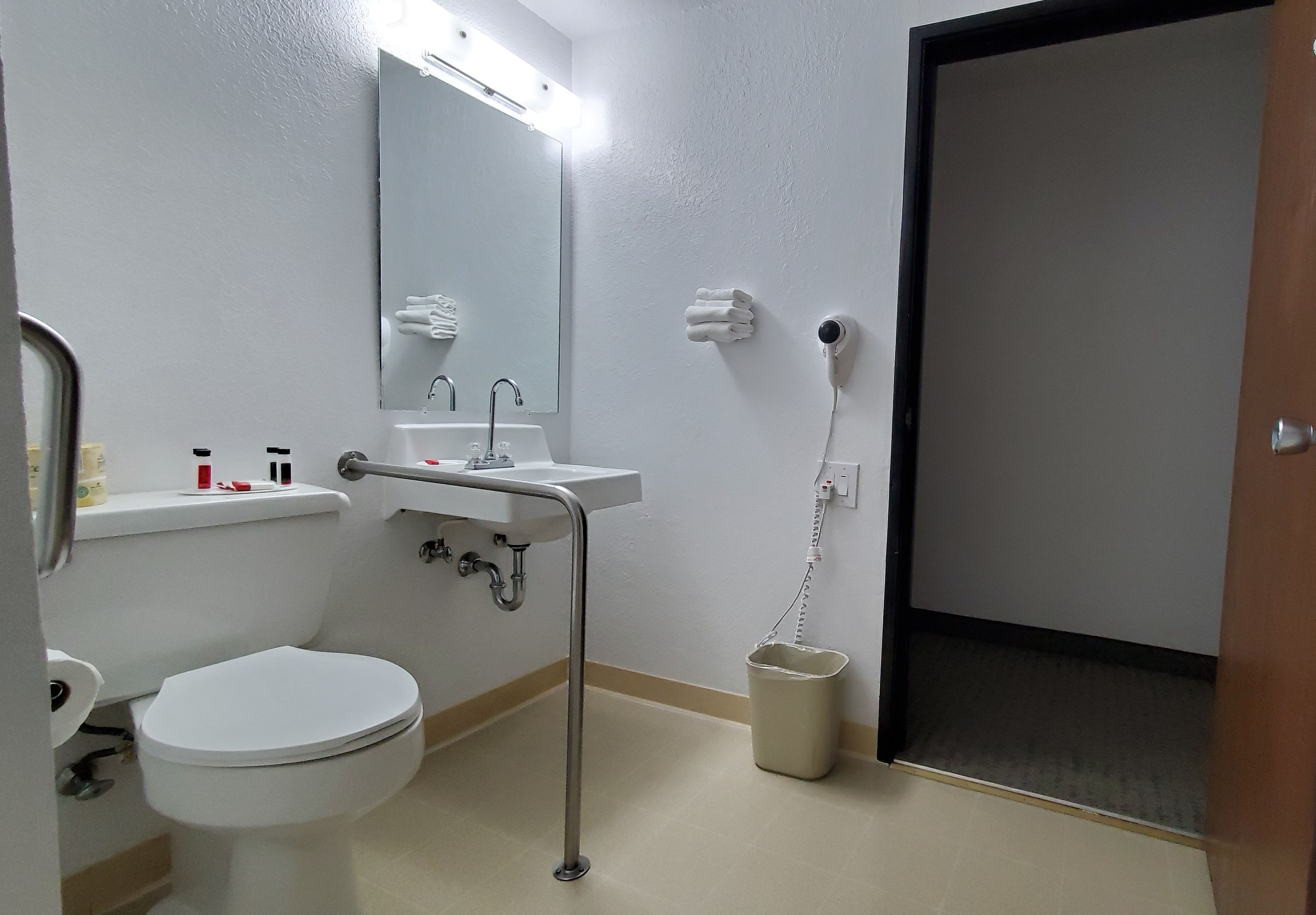 Un baño de hotel estándar con inodoro, lavabo, espejo, toallero y secador de pelo.