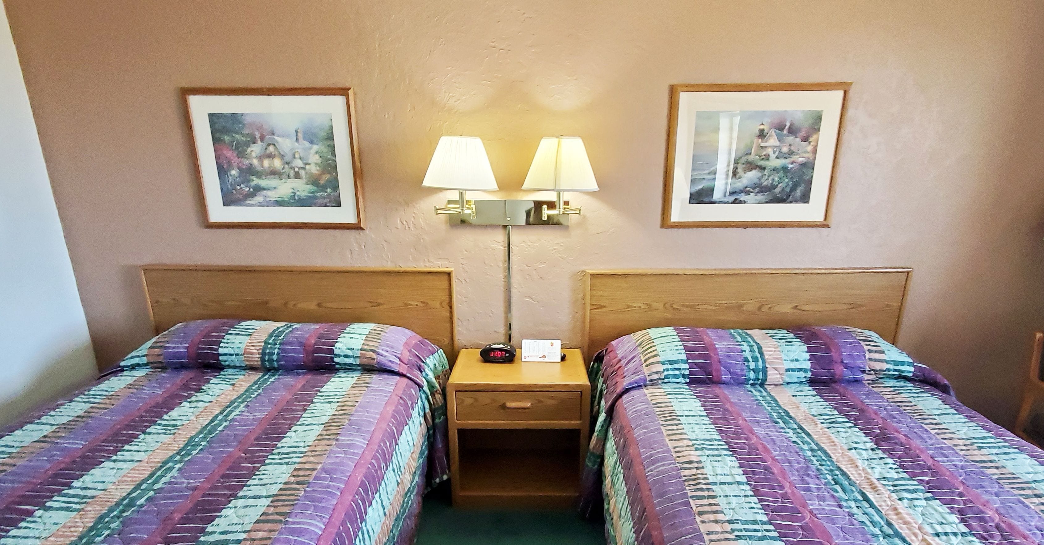 Een hotelkamer met twee bedden, elk met een gestreept sprei, een nachtkastje met een lamp, en twee ingelijste foto’s aan de muur.