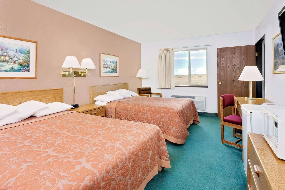 A hotel room with two beds, a desk with a computer, a chair, and a window with curtains.