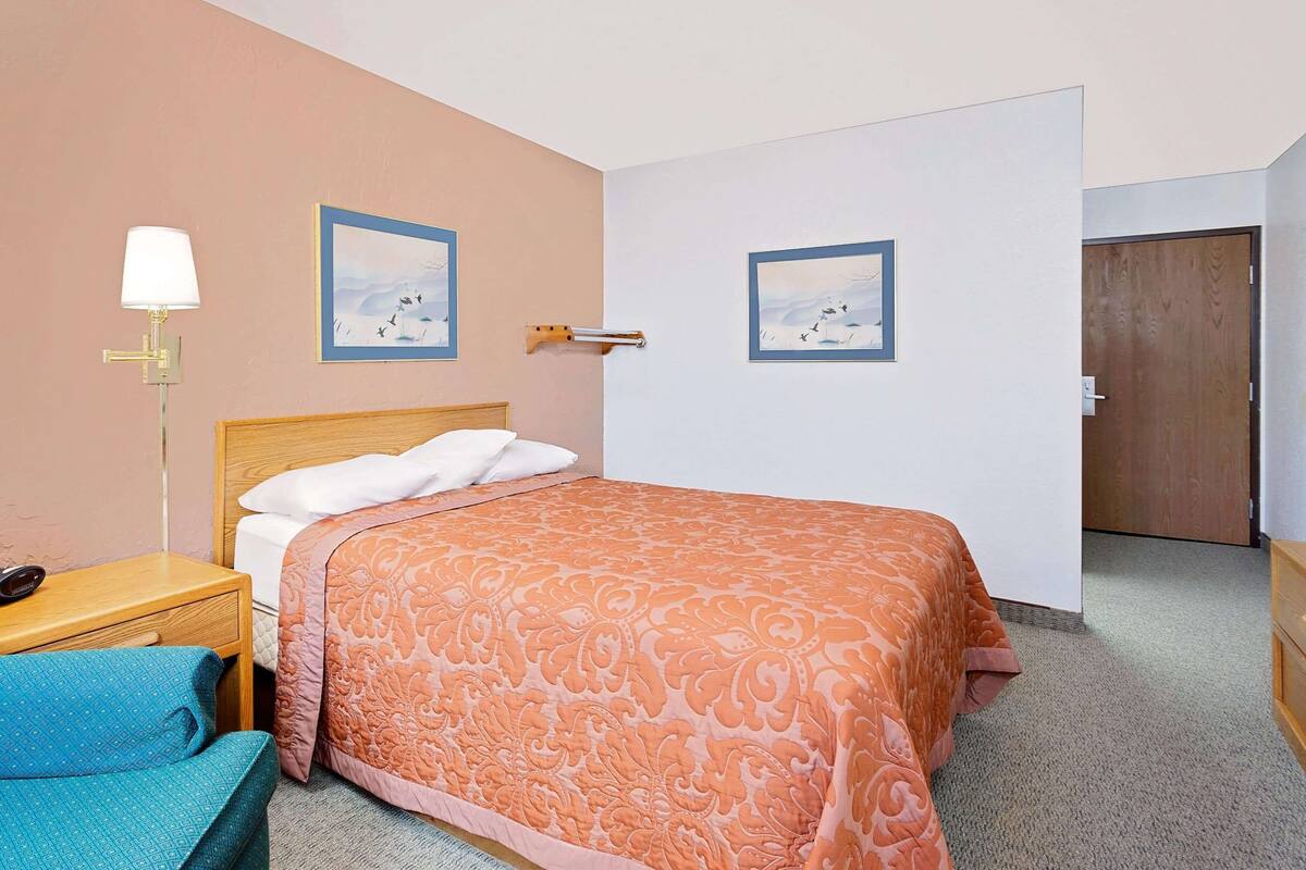 A hotel room with a bed, a bedside table, a lamp, and two framed pictures on the wall.