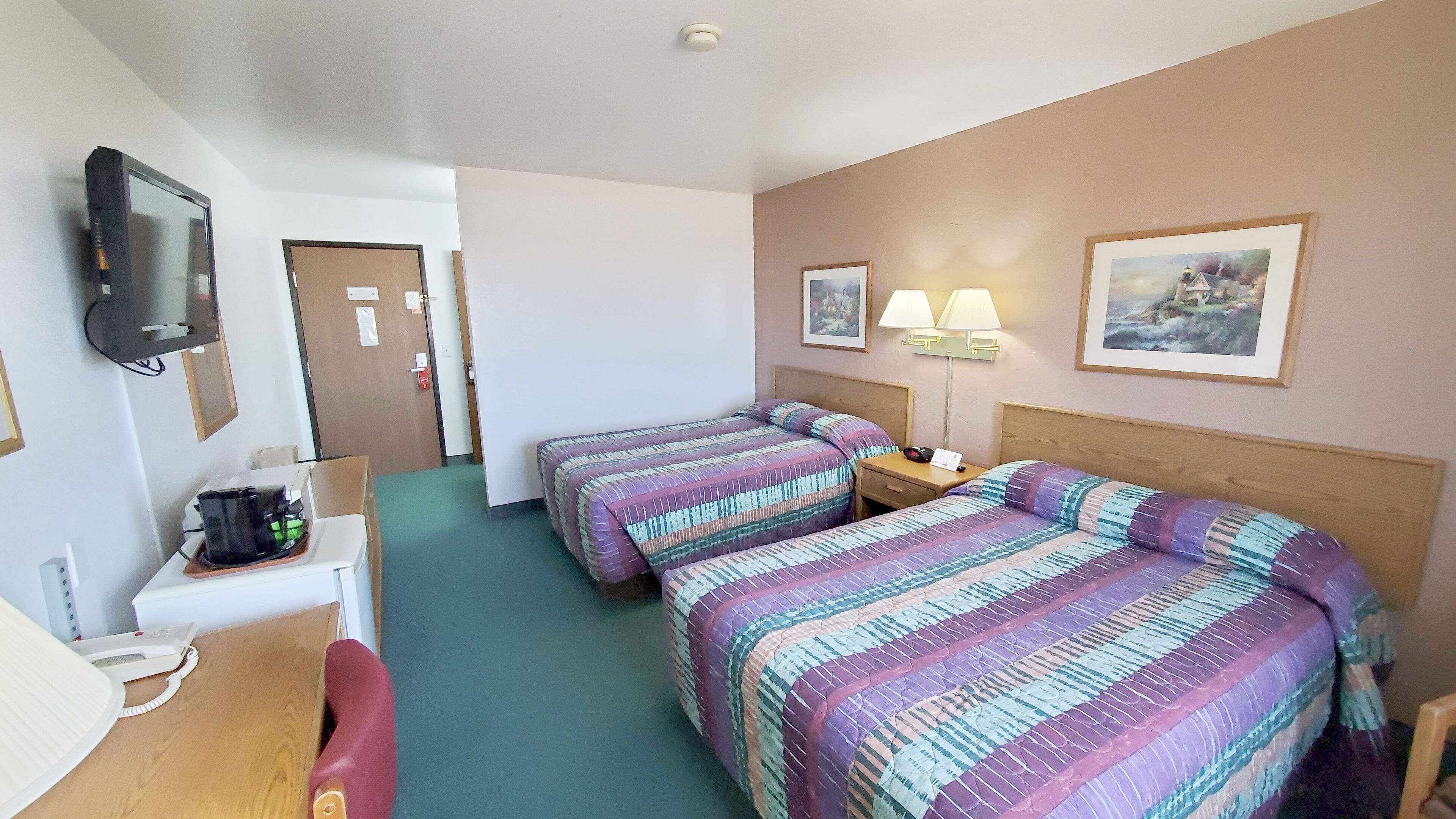A hotel room with two beds, a desk with a telephone, a television, and a painting on the wall.