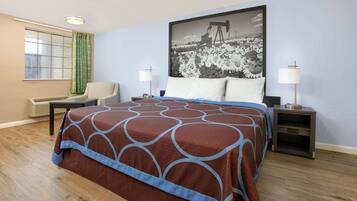 Hotelkamer met een groot bed, twee nachtkastjes, een stoel, een raam met gordijnen en een aan de muur hangend schilderij.