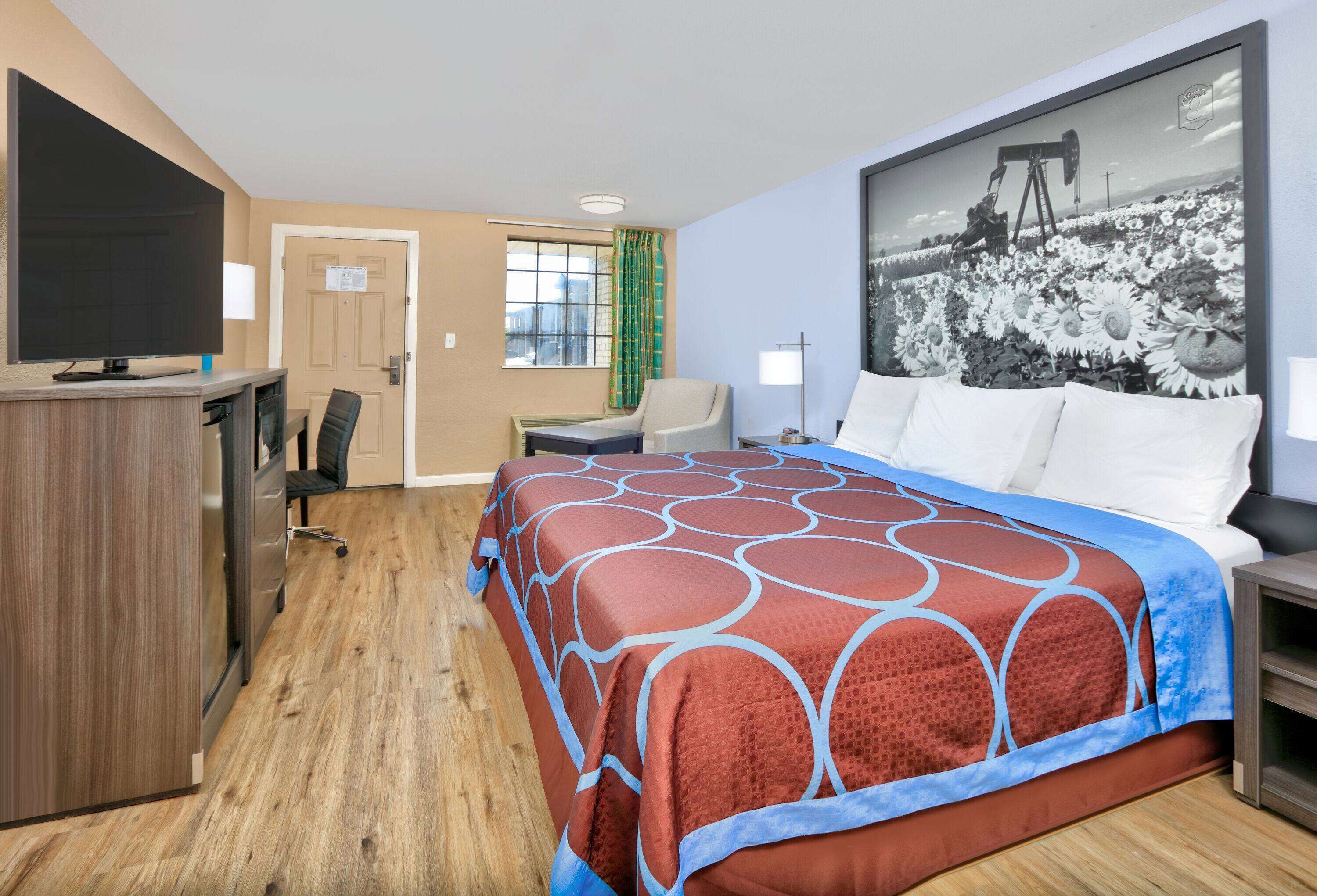 A hotel room with a bed, a desk, a chair, a television, and a large window with curtains.