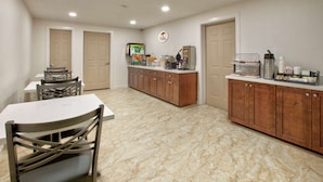A spacious kitchen with a dining table and chairs, a coffee station, and a refrigerator. - Super 8 by Wyndham Victoria / South / Hwy 59 (Victoria)