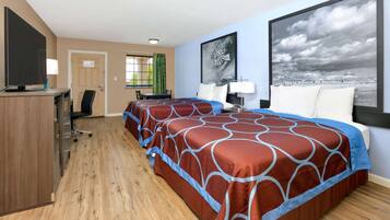 A hotel room with two beds, a desk, a TV, and a large window with a view of the sky.