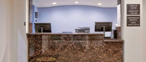 A reception desk with a check-in/out schedule and complimentary breakfast hours.