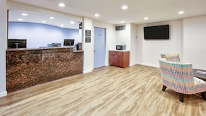 A reception area with a wooden floor, a reception desk, a TV mounted on the wall, and a colorful chair. - Super 8 by Wyndham Victoria / South / Hwy 59 (Victoria)