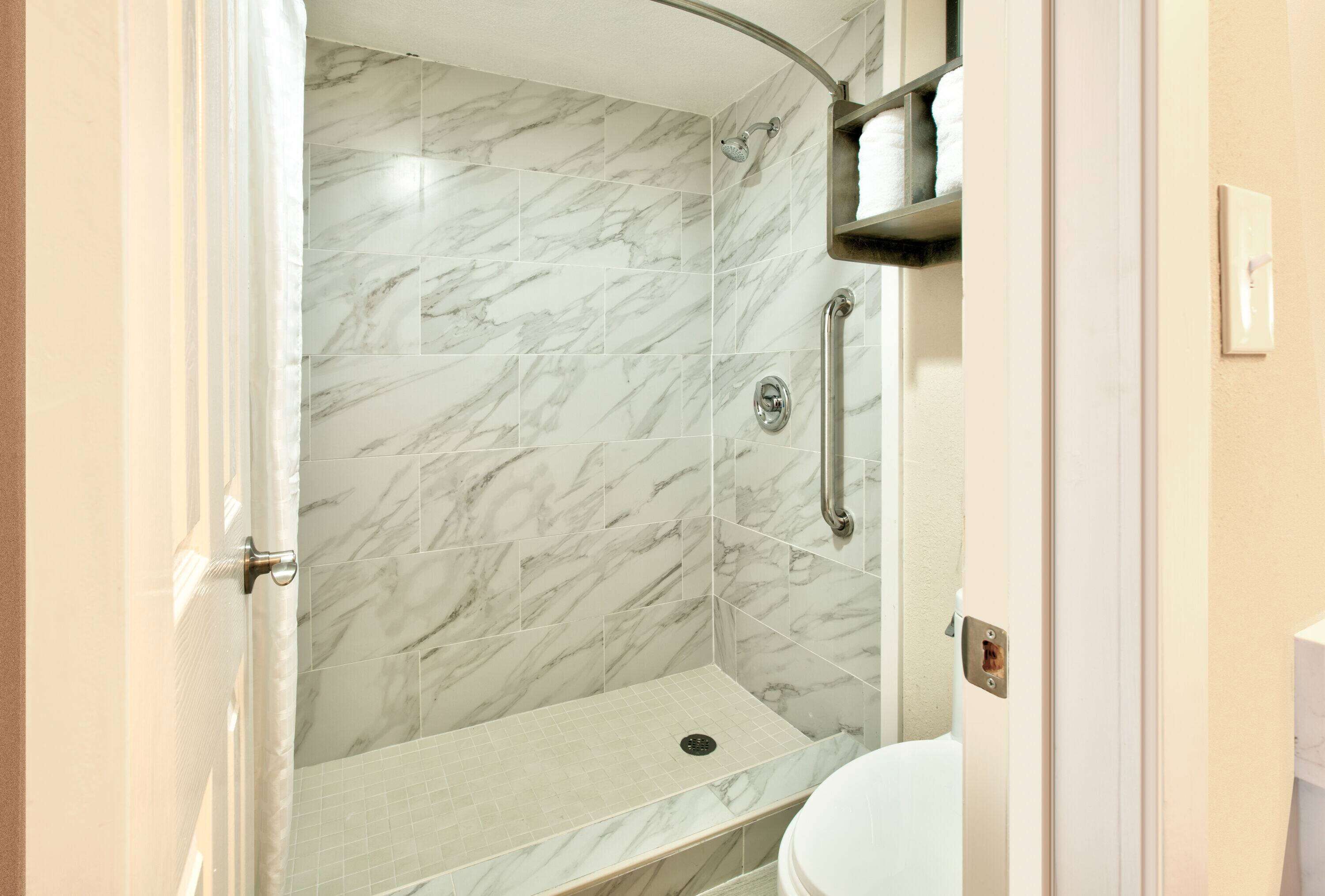 Un baño con ducha, inodoro y azulejos de mármol.