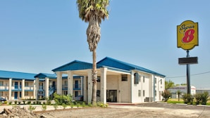 A motel with a blue roof and a palm tree in front. - Super 8 by Wyndham Victoria / South / Hwy 59 (Victoria)