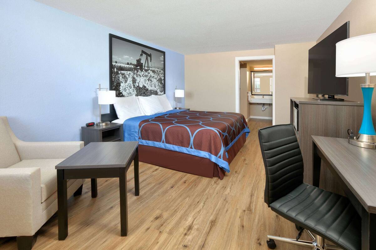 A hotel room with a bed, a desk, a chair, a nightstand, a lamp, and a TV.