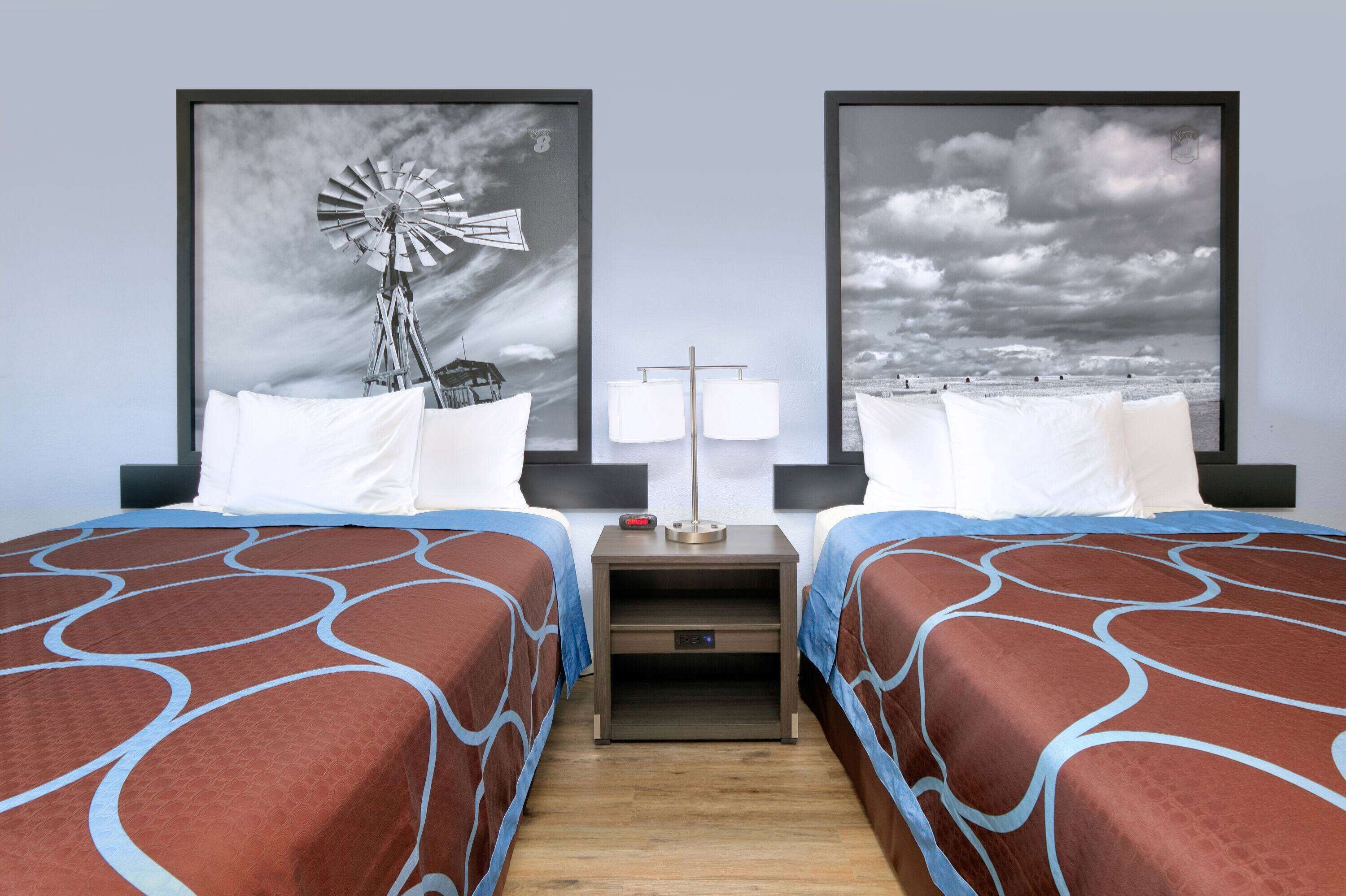 Een hotelkamer met twee bedden, elk met een beddengoed met een patroon, een nachtkastje met een lamp, en twee ingelijste foto’s aan de muur.