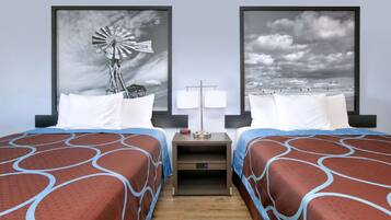 Een hotelkamer met twee bedden, elk met een beddengoed met een patroon, een nachtkastje met een lamp, en twee ingelijste foto’s aan de muur.