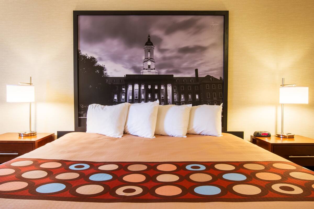 A hotel room with a large bed, two bedside tables with lamps, and a large framed picture of a building on the wall.