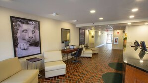 A hotel lobby with a brick-patterned floor, a reception desk, a seating area with white sofas, and a large framed artwork of a lion. - Super 8 by Wyndham State College (State College)