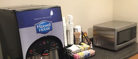 Uma cozinha compacta com cafeteira, micro-ondas e diversos alimentos sobre o balcão.
