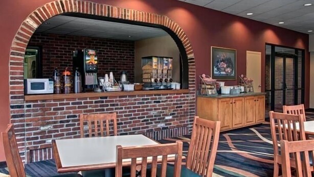 A restaurant with brick walls, wooden tables and chairs, and a counter with various items. - Super 8 by Wyndham State College (State College)