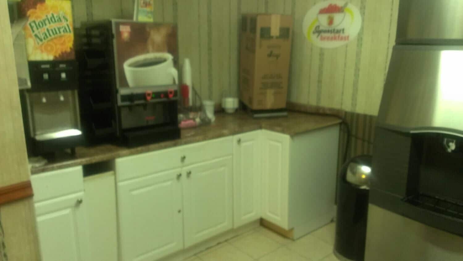 Una cocina con armarios blancos, una cafetera, un cesto de basura y un cartel de Florida's Natural.