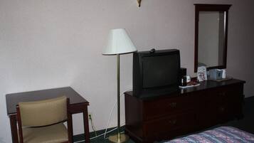 Ein Hotelzimmer mit Bett, Schreibtisch, Stuhl, Fernseher, Kommode, Lampe und Spiegel.