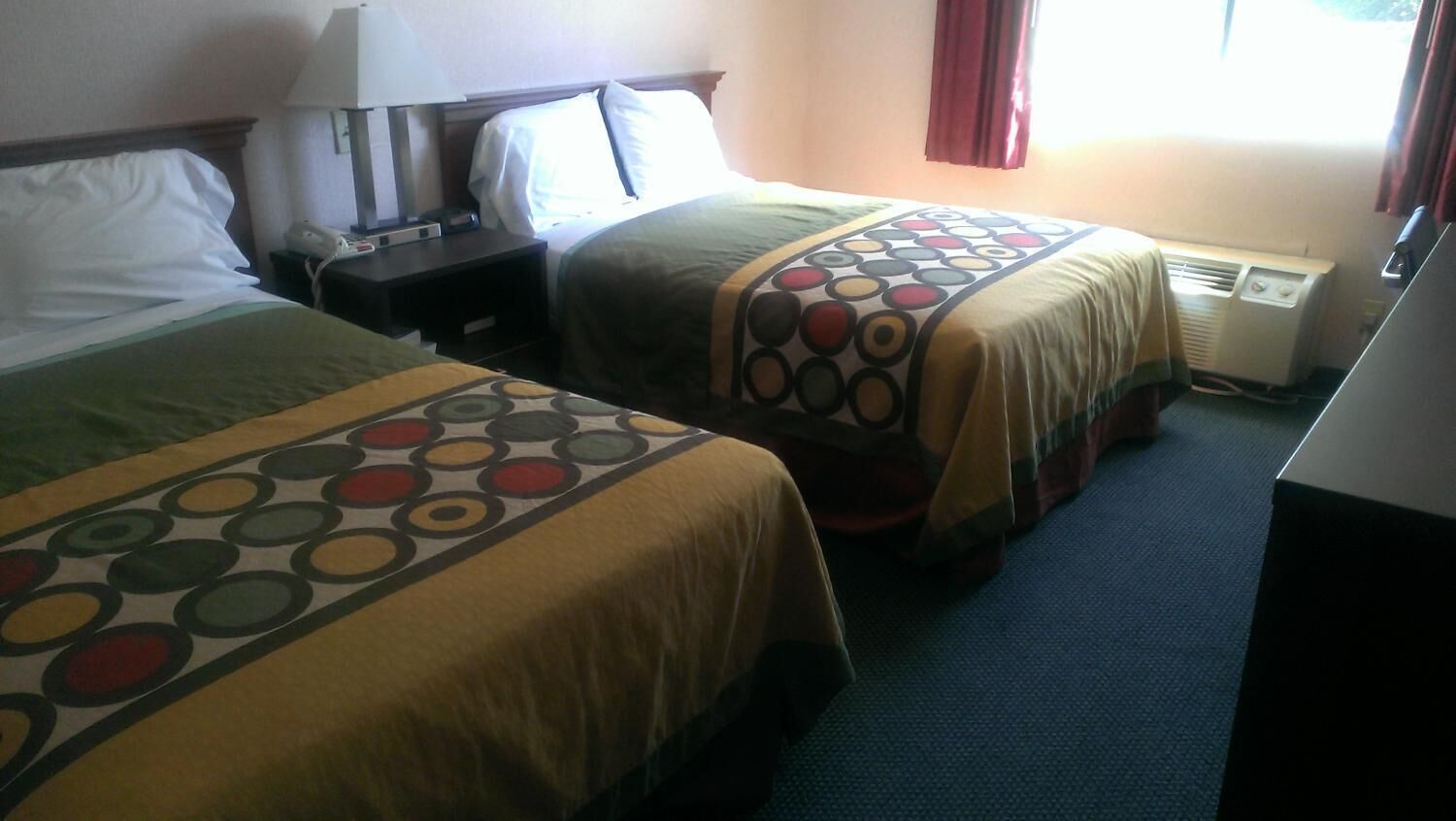 Une chambre d’hôtel avec deux lits, chacun recouvert d’une couvre-lit à motifs, une table de chevet avec une lampe et une fenêtre avec des rideaux.