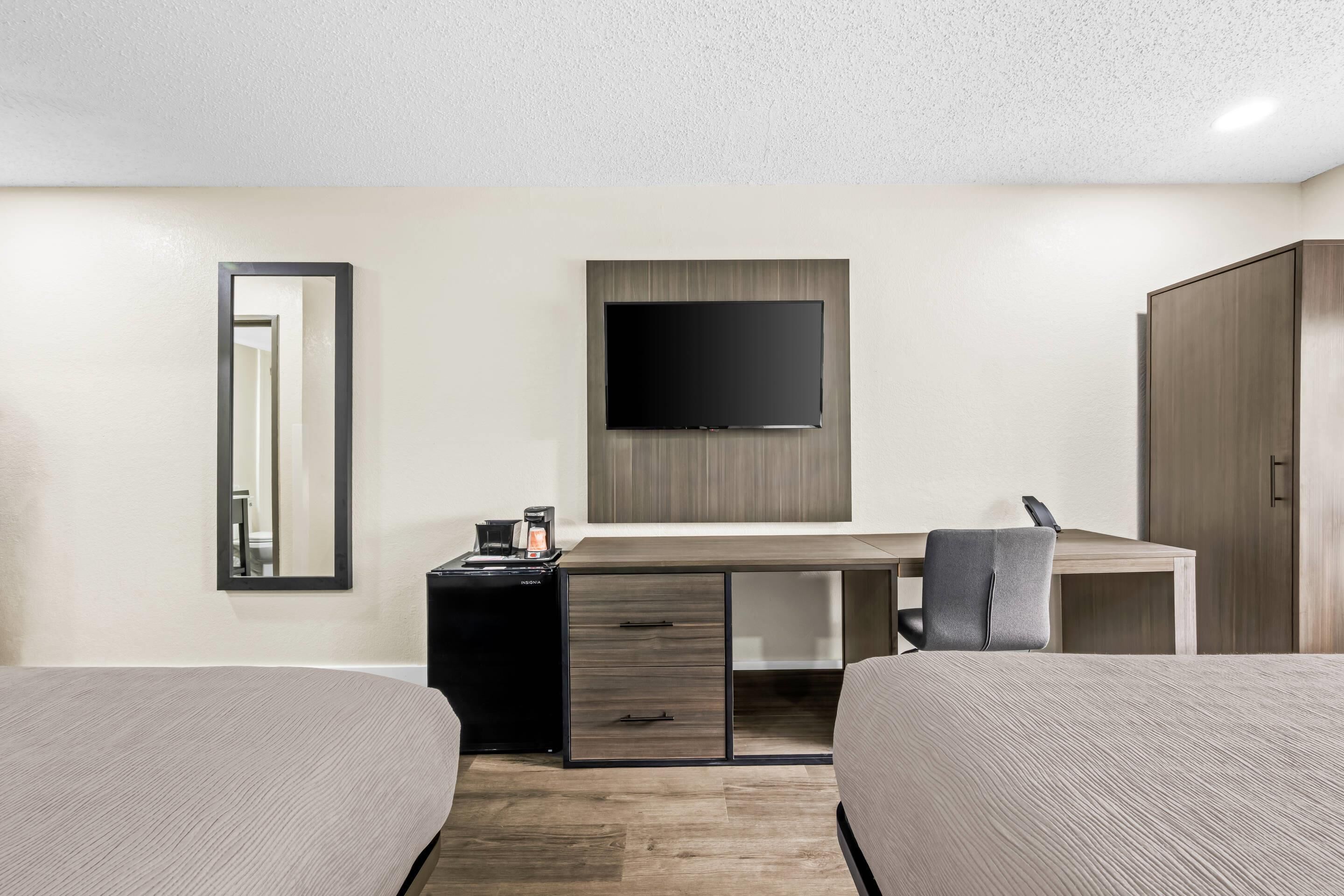 Habitación de hotel con dos camas, un escritorio, televisión, espejo y armario.
