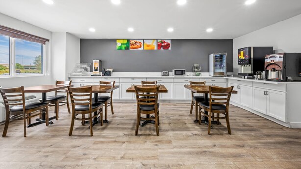 Une cuisine moderne avec des meubles blancs, des tables à manger en bois et des chaises. On y trouve quatre appareils fixés au mur et une grande fenêtre qui laisse entrer la lumière naturelle.