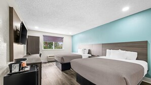 Une chambre d’hôtel avec deux lits, un bureau avec une machine à café, un téléviseur fixé au mur et une fenêtre donnant sur la verdure.
