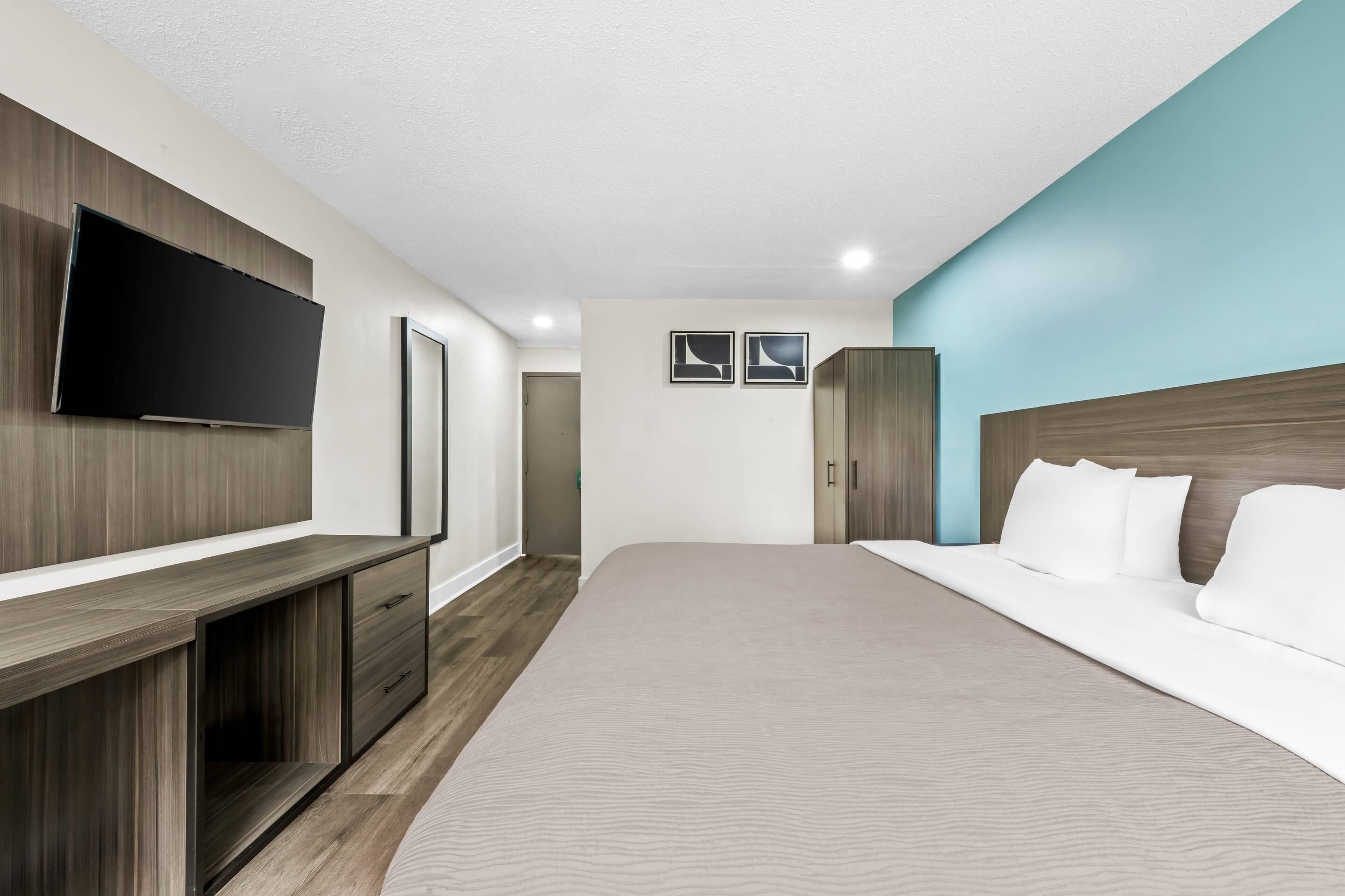 Una habitación de hotel moderna con una cama grande, un televisor montado en la pared, un armario y una puerta que da a un baño.