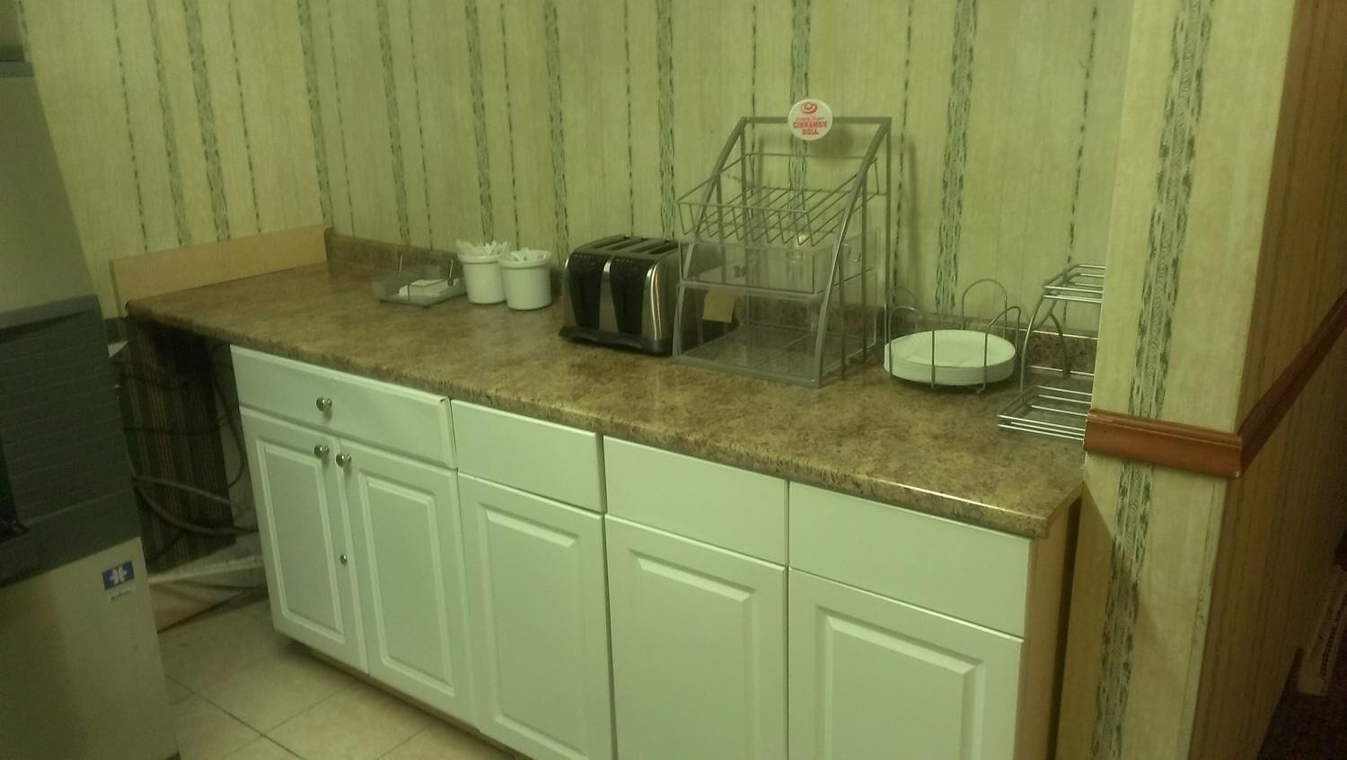 A kitchen with white cabinets, a granite countertop, a toaster, a coffee maker, and a small refrigerator.