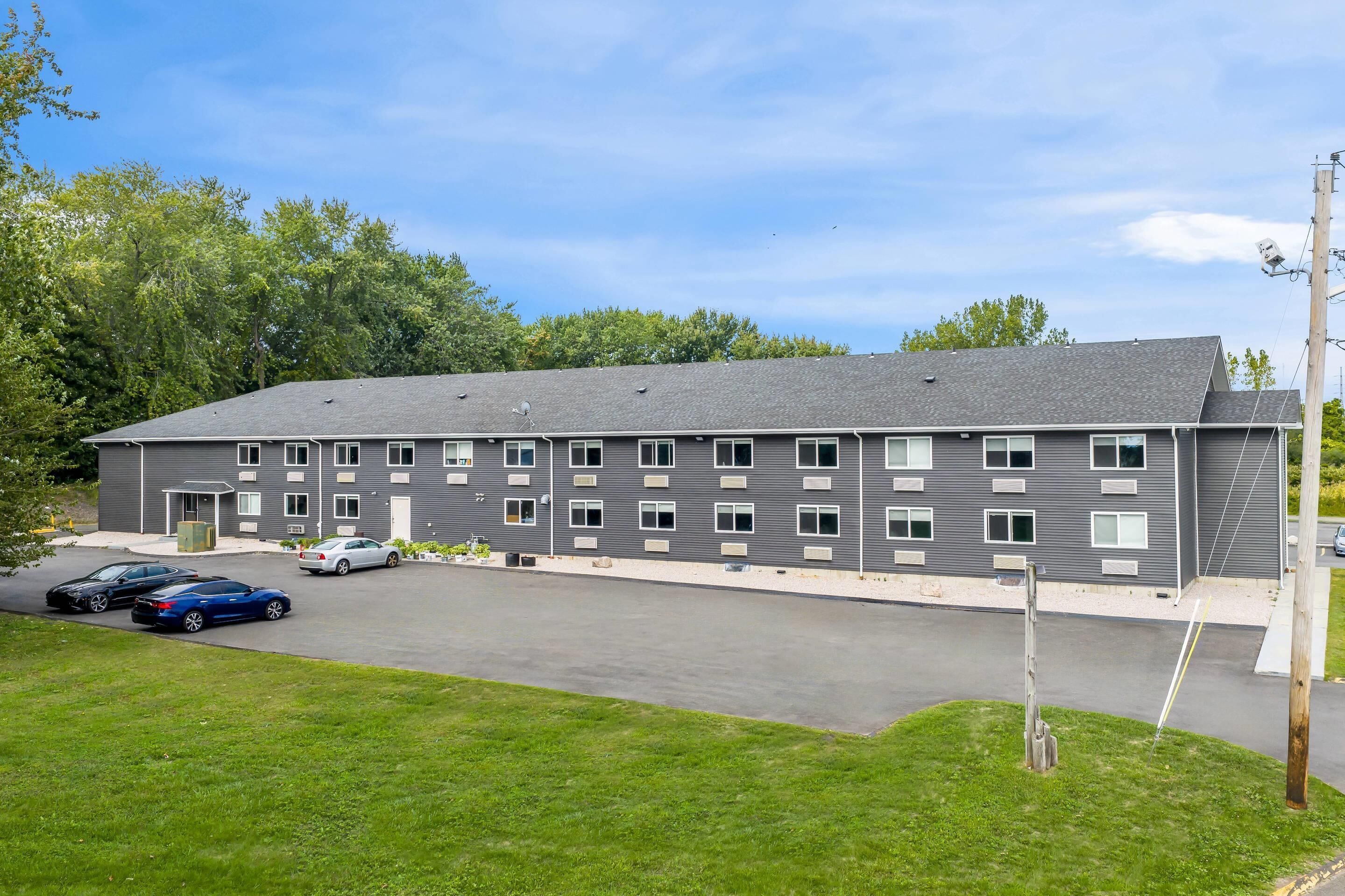 A multi-story building with a flat roof, several windows, and a parking lot with cars.