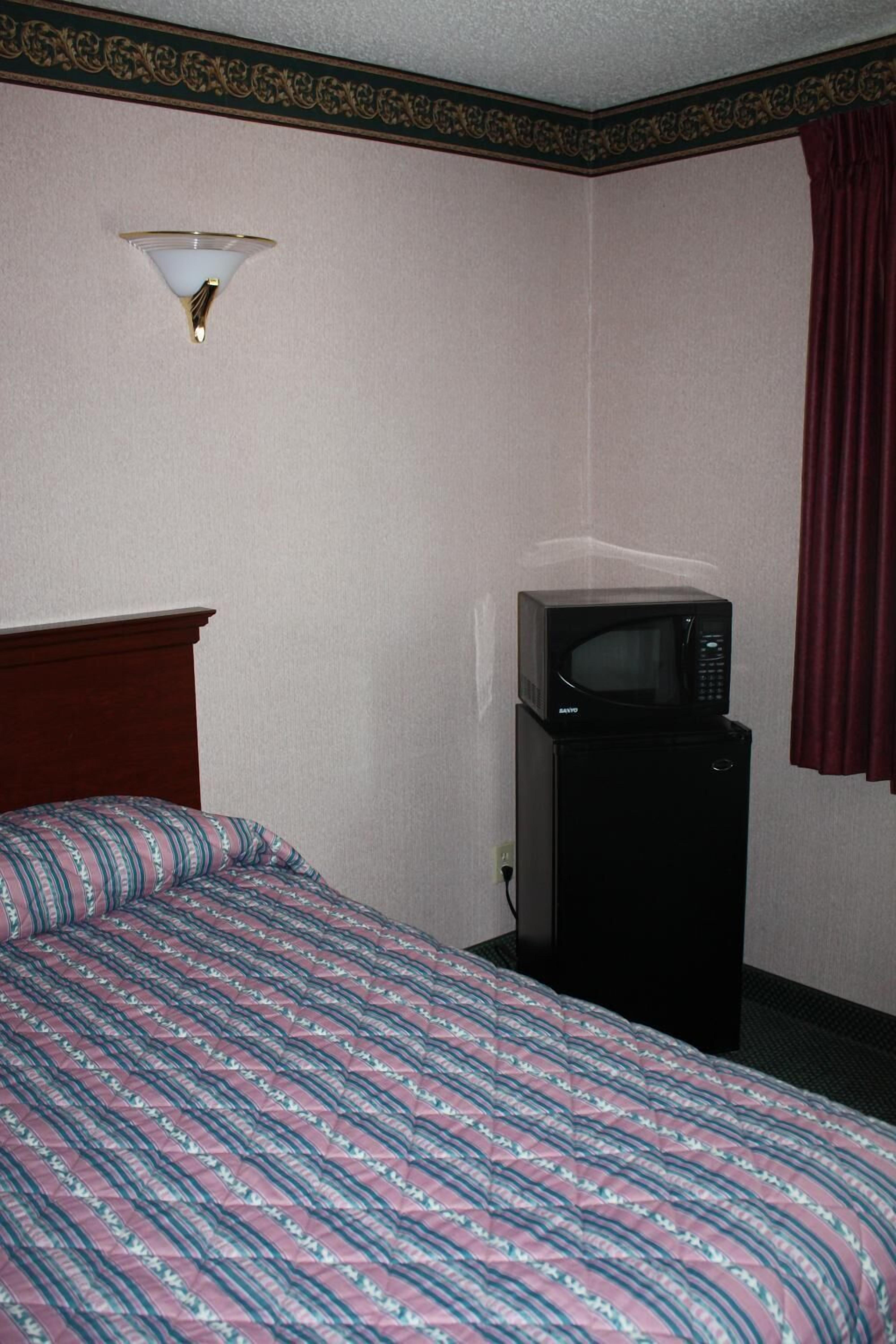 A hotel room with a bed, a microwave, and a wall-mounted light fixture.
