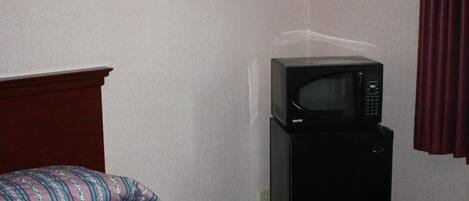 A hotel room with a bed, a microwave, and a wall-mounted light fixture.
