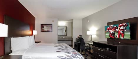 Una habitación de hotel con cama, mesitas de noche, escritorio, silla, televisor y espejo.