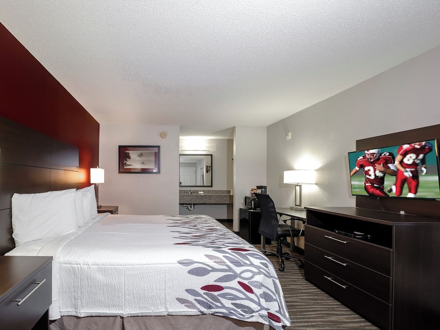 A hotel room with a bed, bedside tables, a desk, a chair, a television, and a mirror.