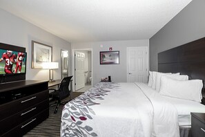 A hotel room with a bed, a desk with a TV, a chair, a desk lamp, and a framed picture on the wall. - Red Roof Inn Defuniak Springs (De Funiak Springs)