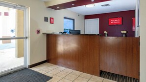 A reception area with a wooden reception desk, a fire alarm, a 'Free Wi-Fi All Rooms' sign, and a door leading outside. - Red Roof Inn Defuniak Springs (De Funiak Springs)