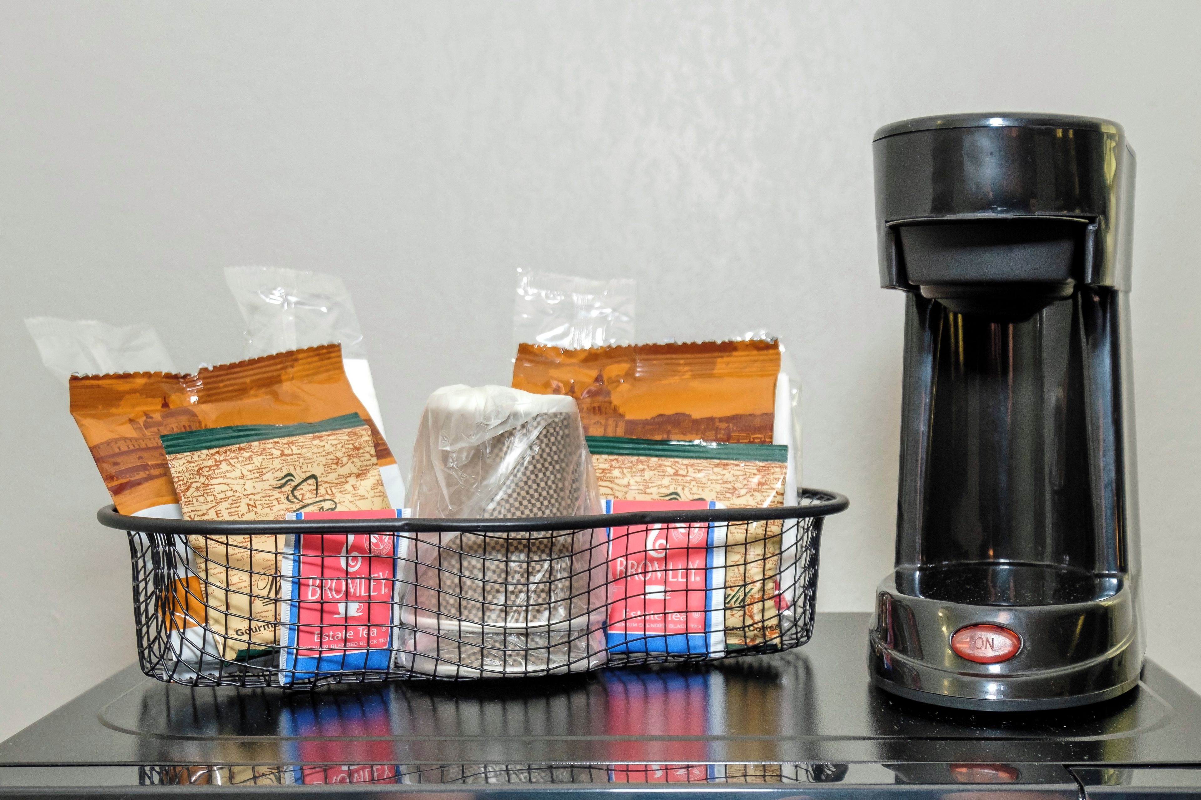 A coffee maker and a basket with tea bags on a table.