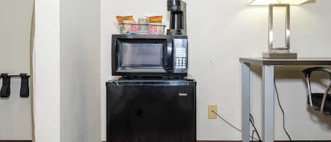 Een kleine keuken met een zwarte koelkast, een magnetron en een koffiezetapparaat.