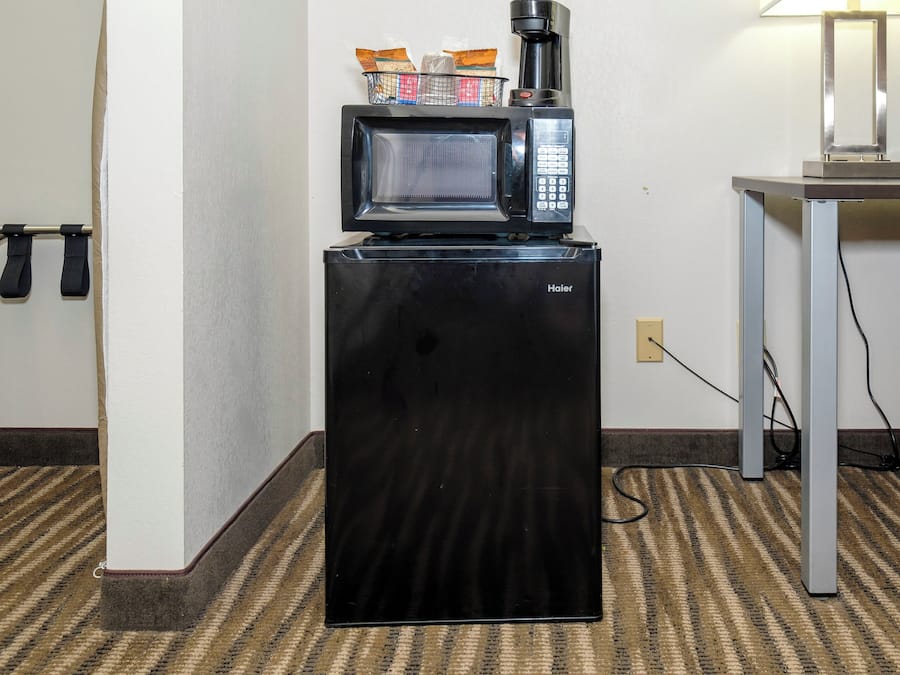 Una kitchenette compacta con un refrigerador negro, un microondas y una cafetera.
