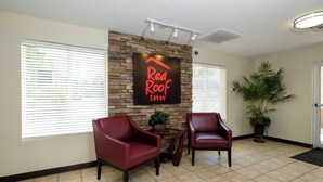 A reception area with a sign reading 'Red Roof Inn' above a stone wall, two leather chairs, a potted plant, and a tiled floor. - Red Roof Inn Defuniak Springs (De Funiak Springs)