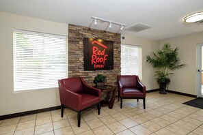 A reception area with a sign reading 'Red Roof Inn' above a stone wall, two leather chairs, a potted plant, and a tiled floor. - Red Roof Inn Defuniak Springs (De Funiak Springs)