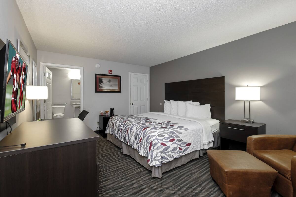 A hotel room with a bed, bedside tables, a desk, a chair, and a TV.