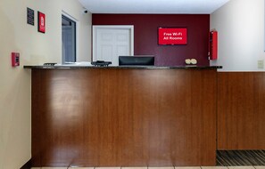 A reception desk with a 'Free Wi-Fi All Rooms' sign, a fire alarm, and a door in the background. - Red Roof Inn Defuniak Springs (De Funiak Springs)