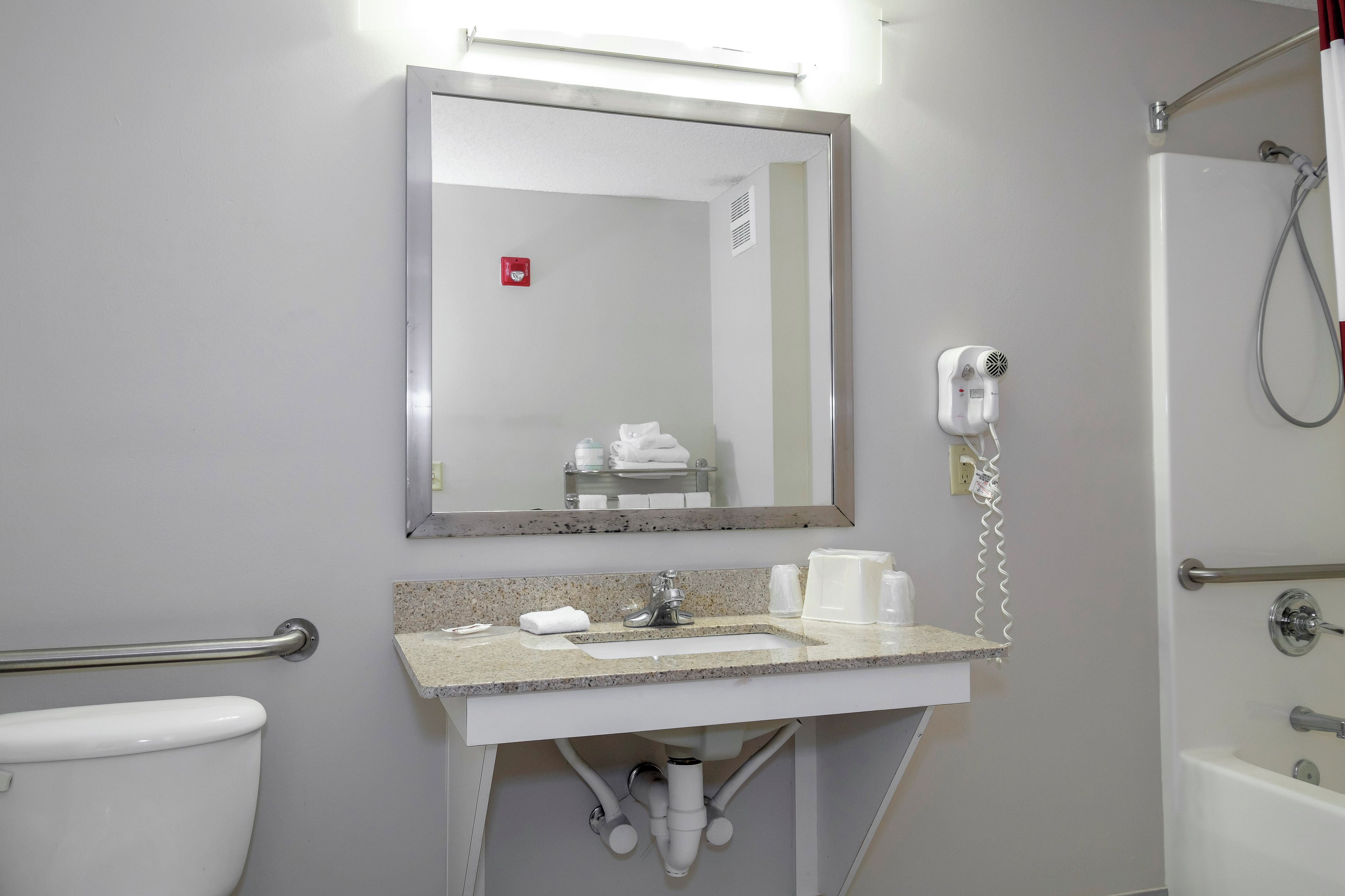 A bathroom with a sink, mirror, towel dispenser, and a hairdryer.